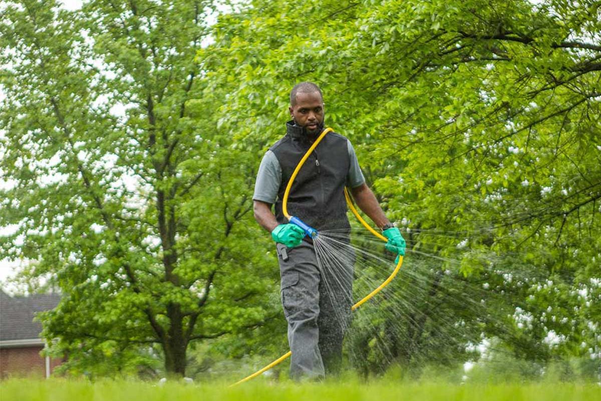 A man spraying a liquid over a lawn using a hose.