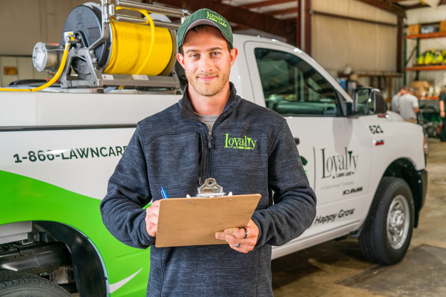 Man standing in front of a Loyalty Lawn Care themed truck while holding a clipboard.