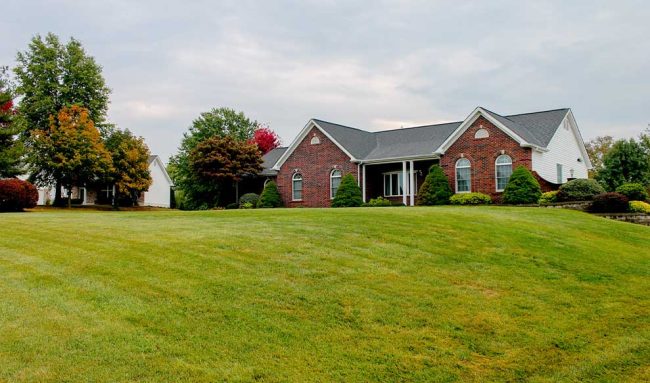 A home in front of a large lawn with trees.