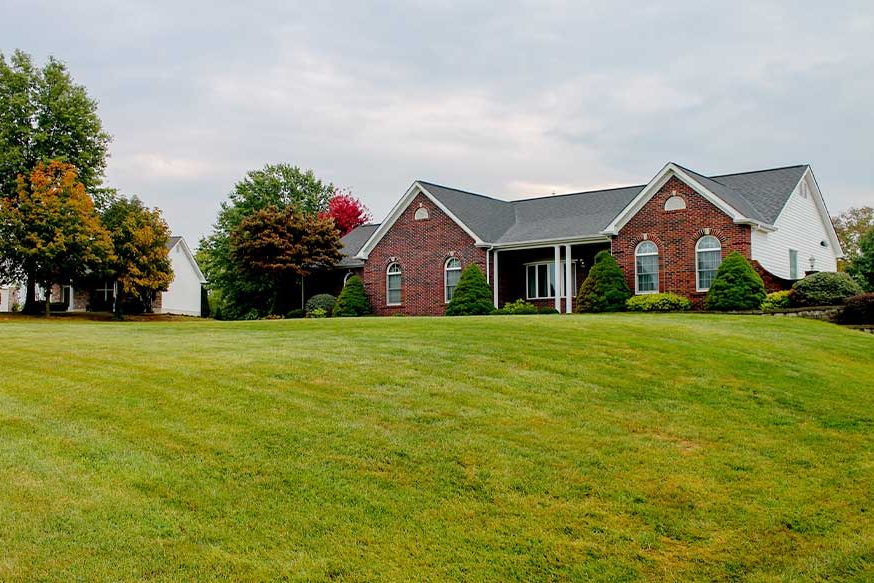 A home in front of a large lawn with trees.